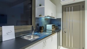 A modern kitchen with a stainless steel sink, a microwave, and a coffee maker. There is a window with a view of the outside, and a door with a frosted glass panel. - Aura Luxury Suites - Olympiada Cozy Getaways (Aristotelis)