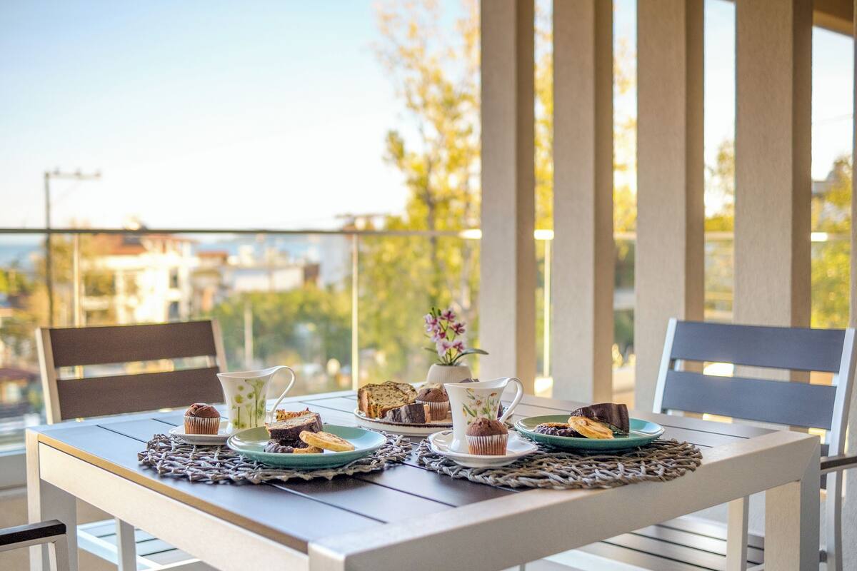 Una mesa lista para una comida, con vista a edificios y árboles al fondo.
