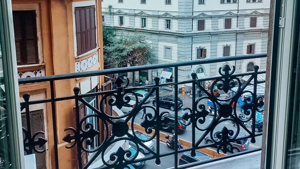 A balcony with wrought iron railings overlooking a street with buildings, including one with a 'KIMBO' sign. - B&B Giosuè (Naples)