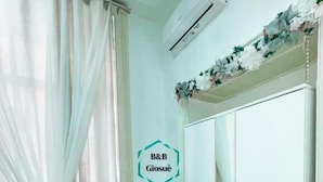 A room with a wooden floor, white walls, a white wardrobe, a small white table, and a white air conditioning unit. - B&B Giosuè (Naples)