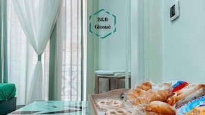 A room with a bed, a window with sheer curtains, a small table with a tray of packaged snacks, and a sign on the wall. - B&B Giosuè (Naples)