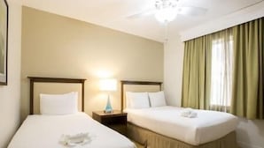Een hotelkamer met twee enkele bedden, een nachtkastje met een lamp, een plafondventilator en een raam met gordijnen.