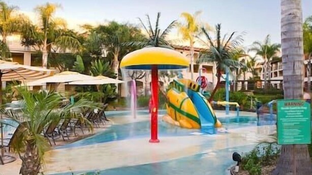 Een waterparkgebied met een grote glijbaan, palmbomen en ligbedden.