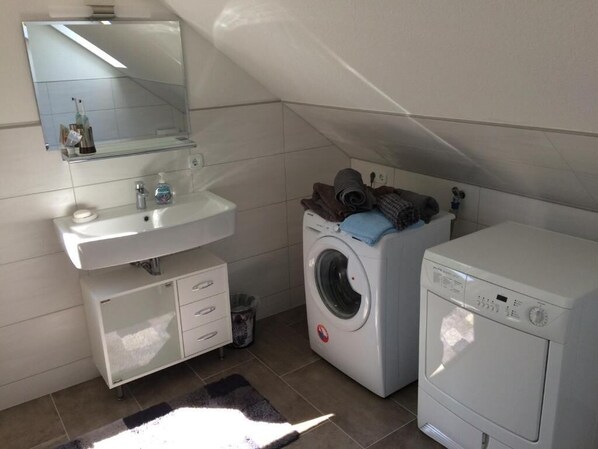 A compact bathroom with a sink, mirror, and two washing machines.