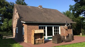 Una casa de ladrillo con tejado de tejas, un patio con mobiliario exterior y un ventanal grande.