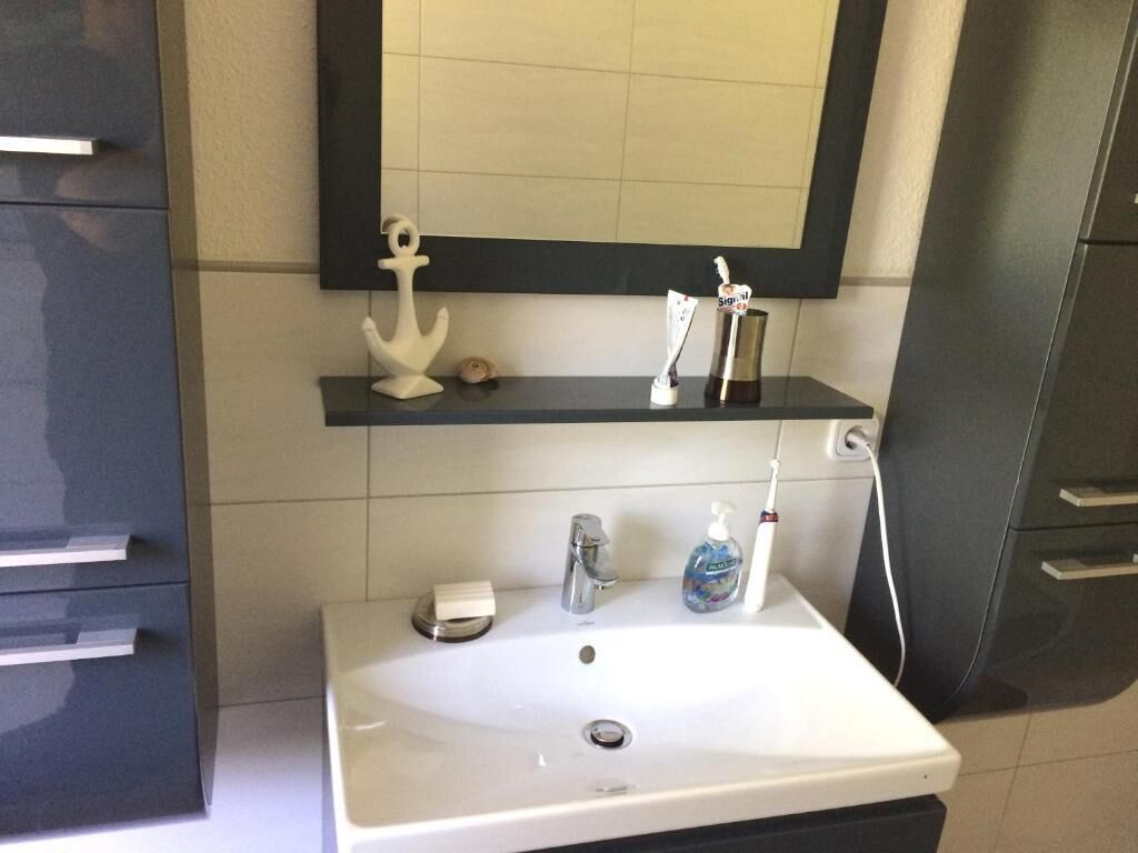 A bathroom with a white sink, a mirror, a soap dispenser, and a toothbrush holder.
