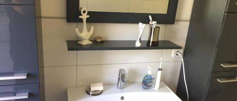 A bathroom with a white sink, a mirror, a soap dispenser, and a toothbrush holder.