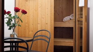 A wooden sauna room with a glass door, a small table with chairs, and a vase with red roses.