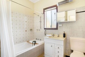 A bathroom with a bathtub, a sink, a toilet, and a mirror. - The Peach Tree 2 Bed Home (Elizabeth Vale)