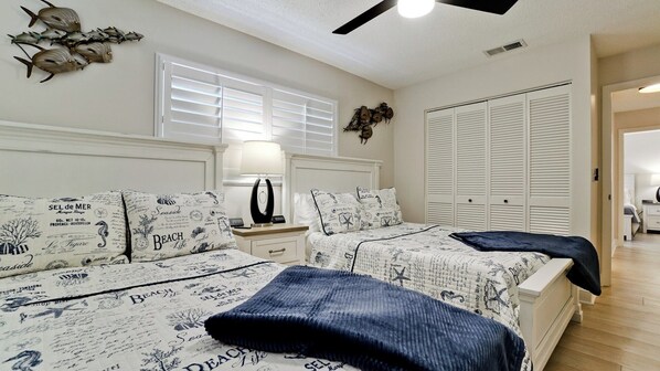 Un dormitorio con dos camas, una mesita de noche, una lámpara, un ventilador de techo y un armario.