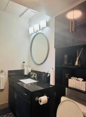 Bathroom features a vanity, round mirror, toilet, and shelf with toiletries.