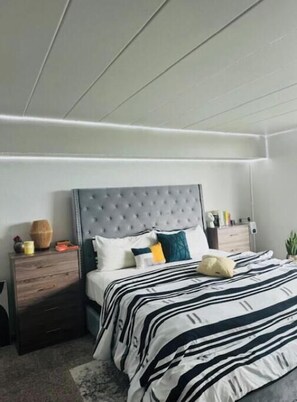 Relax in this serene bedroom with a large bed, tufted headboard, and a nightstand with drawers.