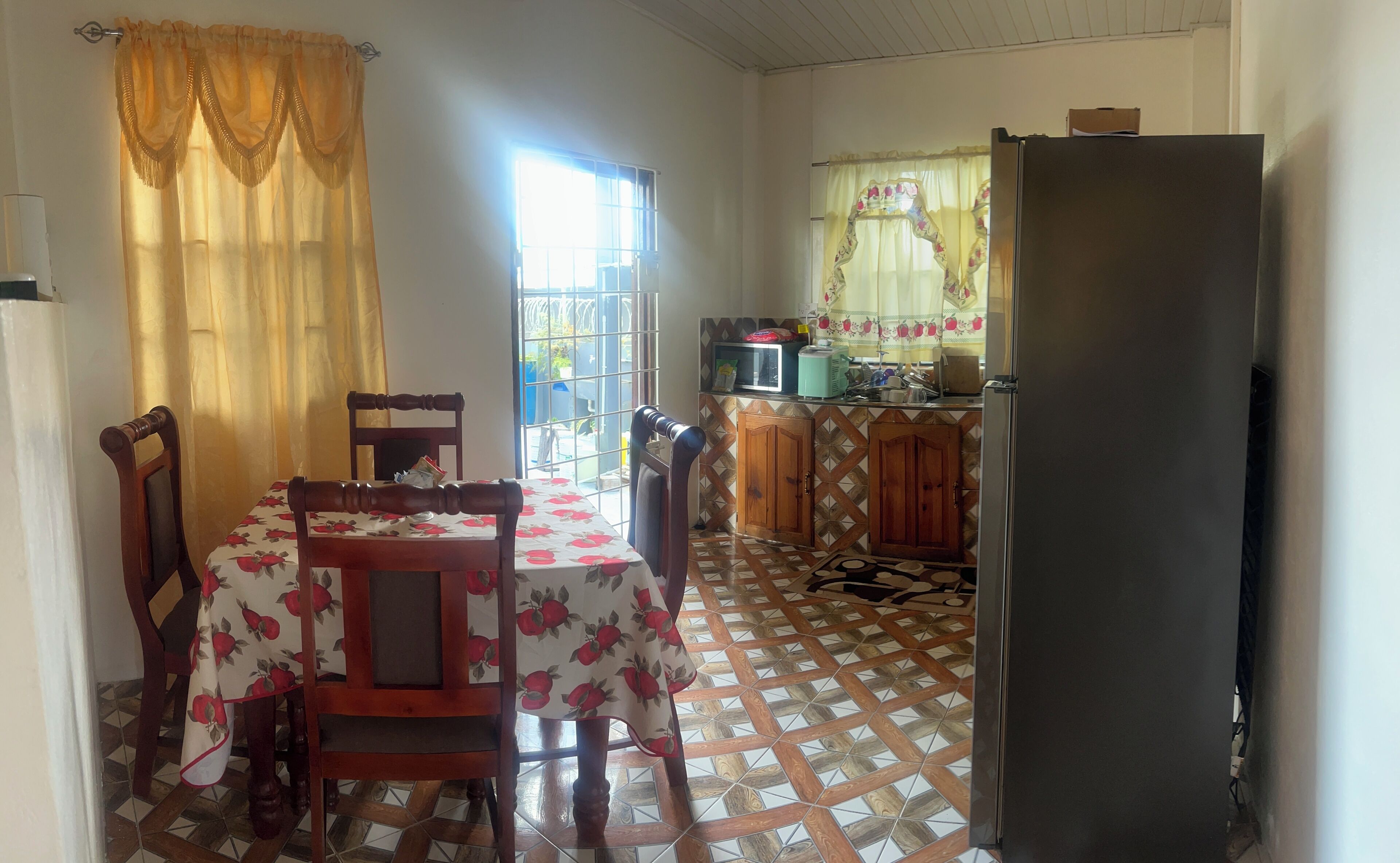 Une cuisine équipée d’une table à manger, de chaises, d’un réfrigérateur et d’une fenêtre avec des rideaux.