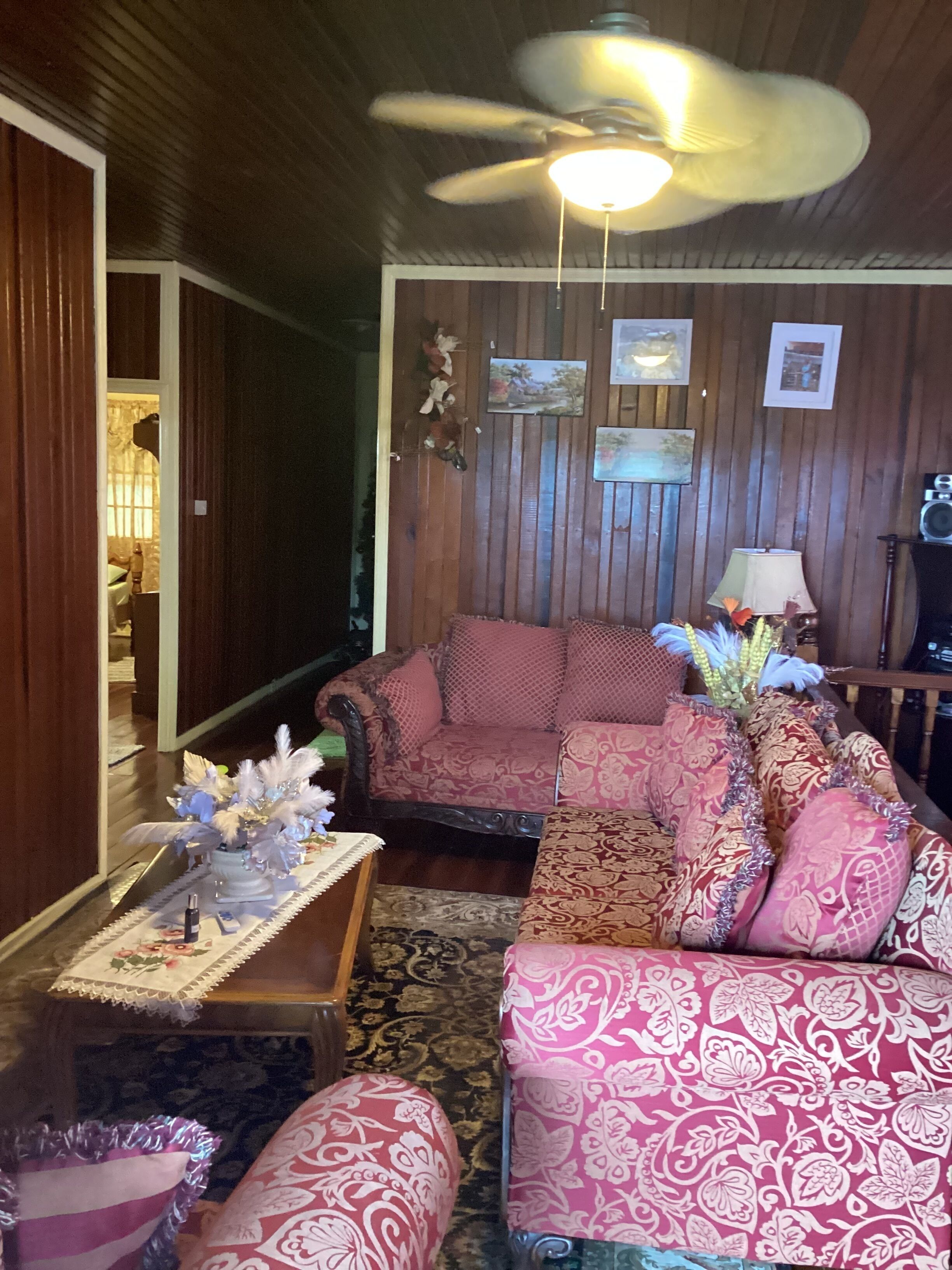 A cozy living room with a wooden ceiling, a ceiling fan, and a sofa set.