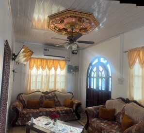 A living room with patterned sofas, a ceiling fan, and a decorative ceiling.