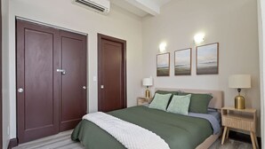 Une chambre à coucher comprenant un lit, deux tables de chevet, un climatiseur fixé au mur et trois tableaux encadrés.