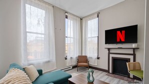 Un salon moderne avec un canapé de couleur turquoise, une table basse en bois, une cheminée et un téléviseur fixé au mur.