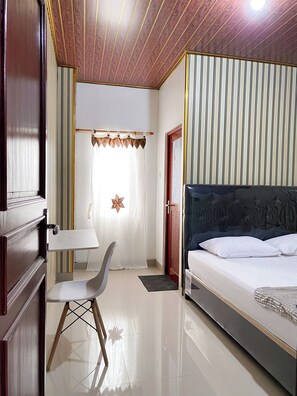 A bedroom with a bed, a chair, a desk, a window with curtains, and a star decoration. - d'WF Hotel (Kalasan)
