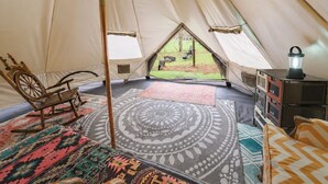 A tent interior with a rocking chair, a patterned rug, a storage unit, and a view of the outdoors. - Boho Off-grid Glamping at Honeysuckle Springs (Cosby)