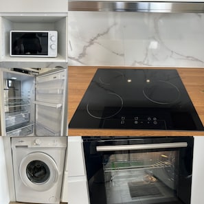 Een keuken met een ingebouwde magnetron, een zwart inductiekookplaat, een ingebouwde oven en een wasmachine.
