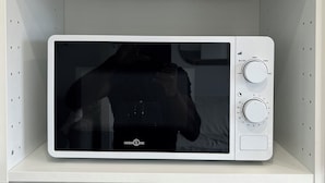 Un four à micro-ondes blanc est posé sur une étagère blanche dans une cuisine dont les comptoirs sont en marbre.