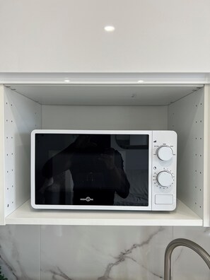 Een witte magnetron op een witte plank in een keuken met marmeren aanrecht.