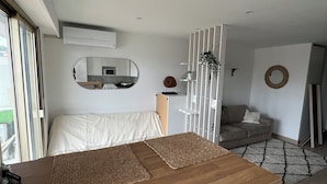 Un salon moderne avec une table basse en bois, un canapé, une table à manger et un coin cuisine visible à travers une porte ouverte.