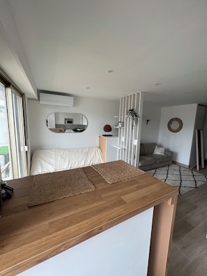 Een moderne woonkamer met een houten salontafel, een bank, een eettafel, en een keuken die zichtbaar is door een open deur.