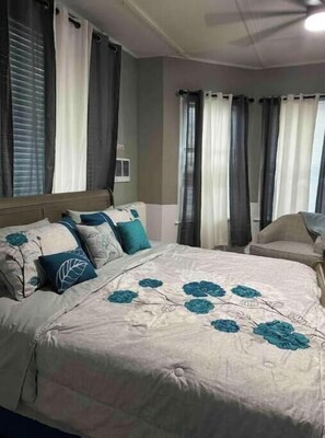 A bedroom with a bed, a chair, and curtains. - Classic King Suite Apartment (Schenectady)