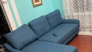 Um sofá azul em um quarto com paredes verde-água e cortina estampada.