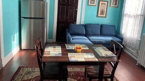 Uma área de refeições com mesa e cadeiras de madeira, um sofá azul e uma geladeira.