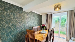 Un coin repas avec une table et des chaises en bois, un vase rempli de fleurs et un papier peint à motifs.
