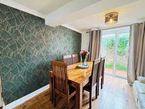 A dining area with a wooden table and chairs, a vase with flowers, and a patterned wallpaper.
