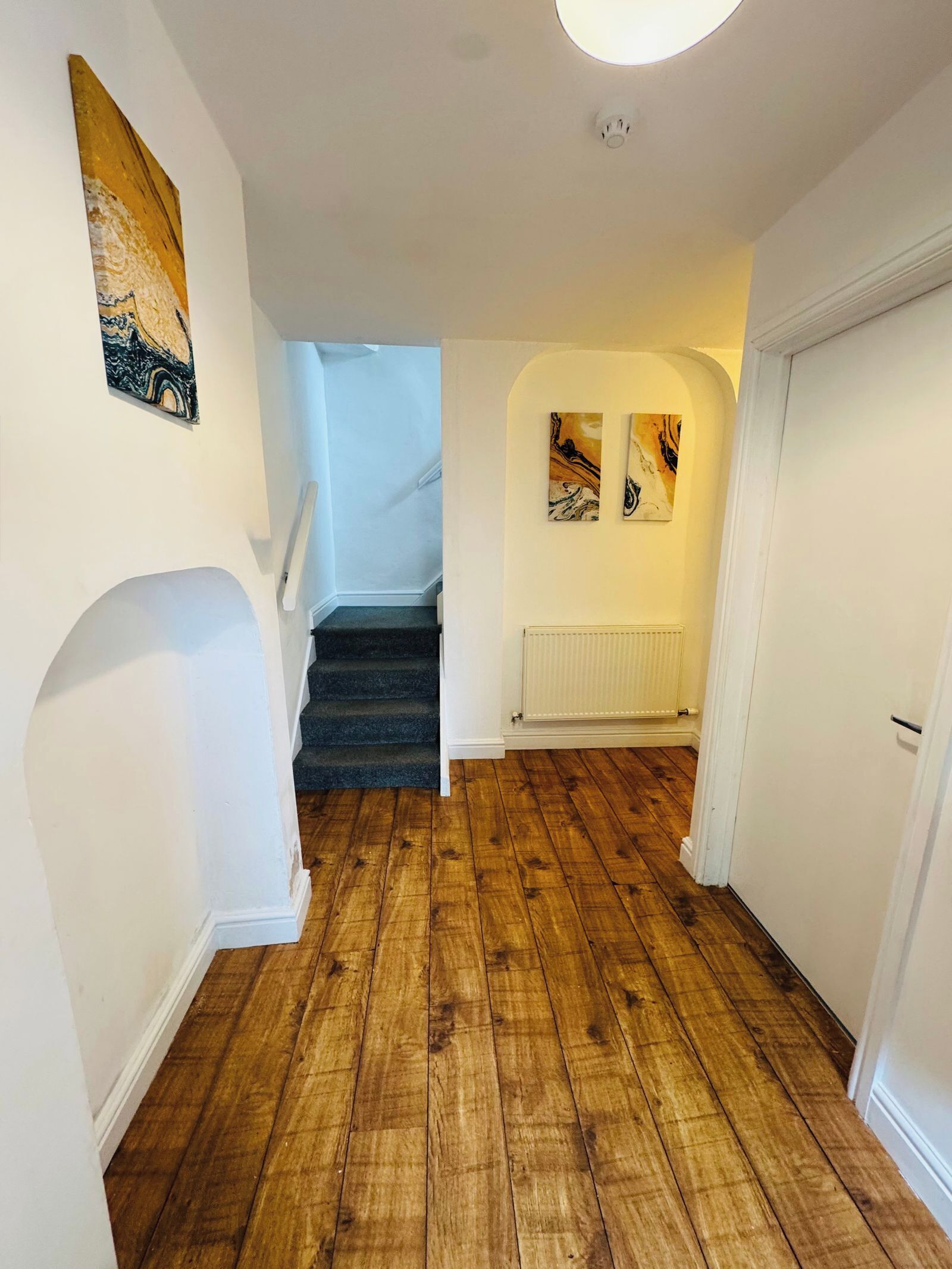 A hallway with wooden flooring, white walls, and a staircase leading to another level.