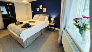 Une chambre à coucher avec un lit, une table de chevet, une lampe et une fenêtre avec des rideaux.