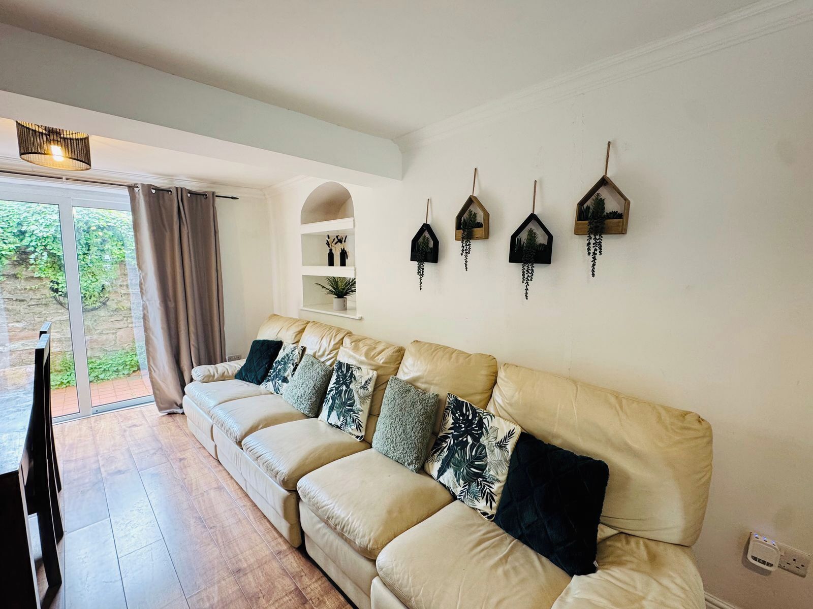 Ein Wohnzimmer mit einem beige-farbenen Sofa, einem Flachbildfernseher und einer Schiebetür zu einem Garten.
