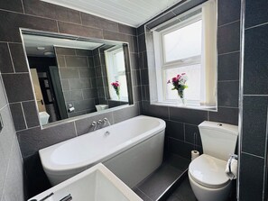 A modern bathroom with a freestanding bathtub, a toilet, and a large mirror.