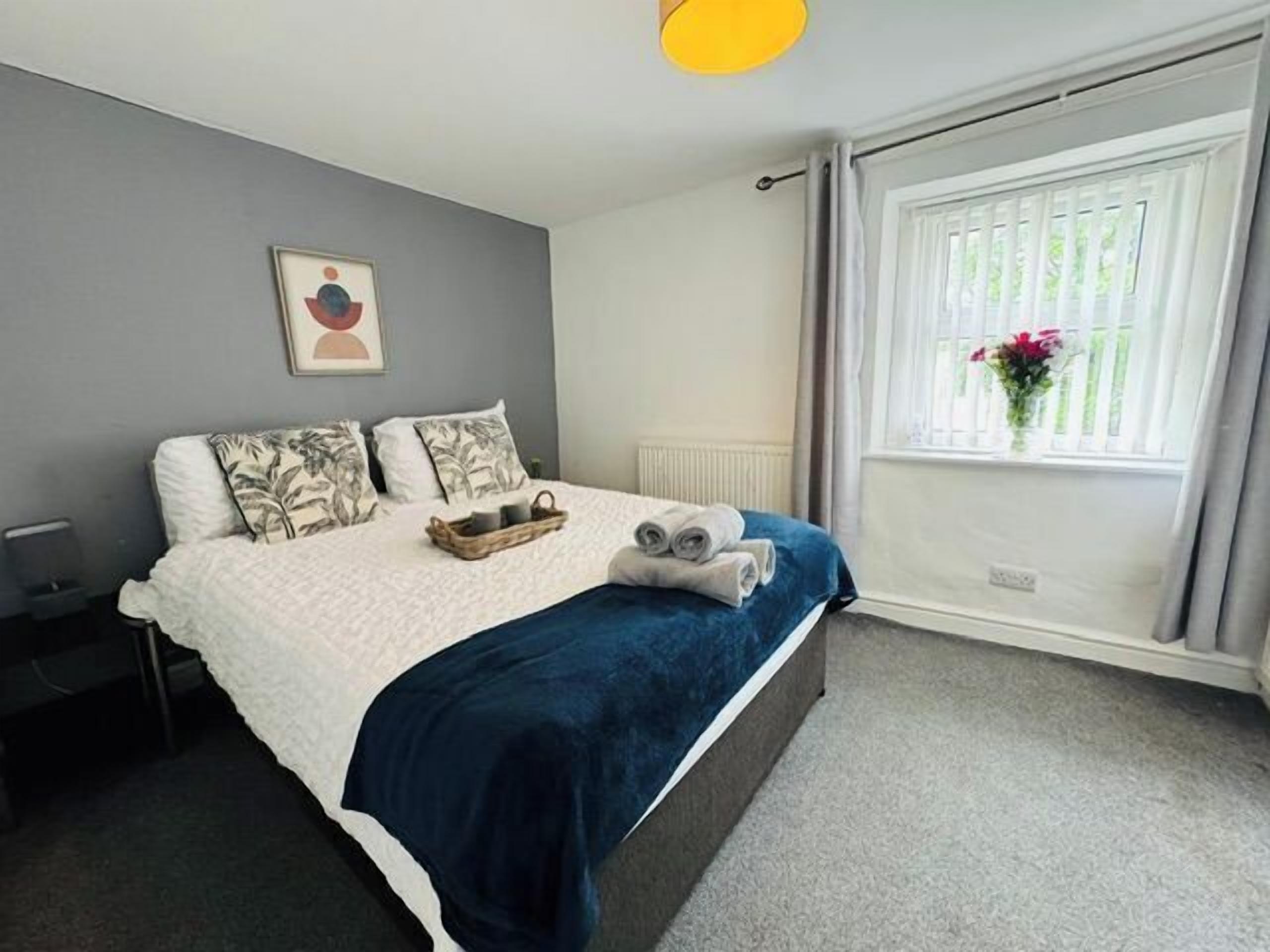 Ein Schlafzimmer mit einem Bett, Kissen, einem Nachttisch, einem Fenster mit Vorhängen und einem Wandbild.
