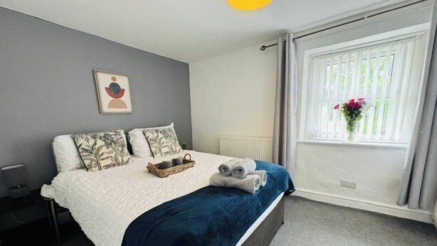Une chambre à coucher avec un lit, des oreillers, une table de chevet, une fenêtre avec des rideaux et un tableau accroché au mur.