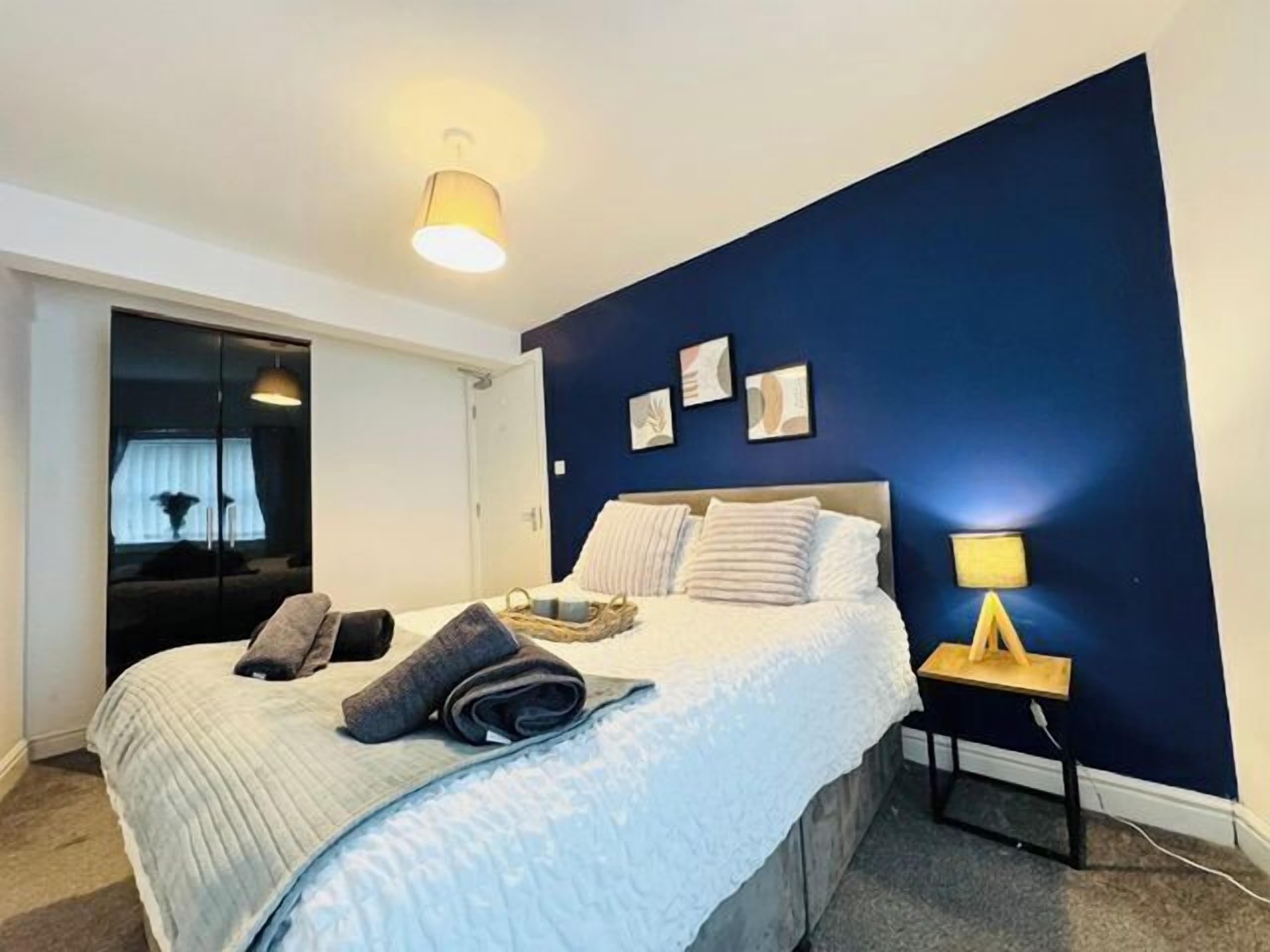 A bedroom with a bed, bedside table, lamp, and wall art.