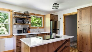 A modern kitchen with wooden cabinets, a stainless steel refrigerator, a built-in microwave, and a large island with a kettle. - Waterfront retreat with fireplace 3 miles from Whiteface & The North Pole (Wilmington)