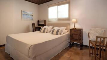 Une chambre à coucher avec un grand lit, une table de chevet, une lampe, une chaise, une fenêtre et un tableau au mur.