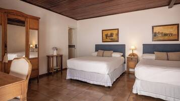 Quarto de hotel com duas camas, um guarda-roupa de madeira, uma escrivaninha e uma mesinha.