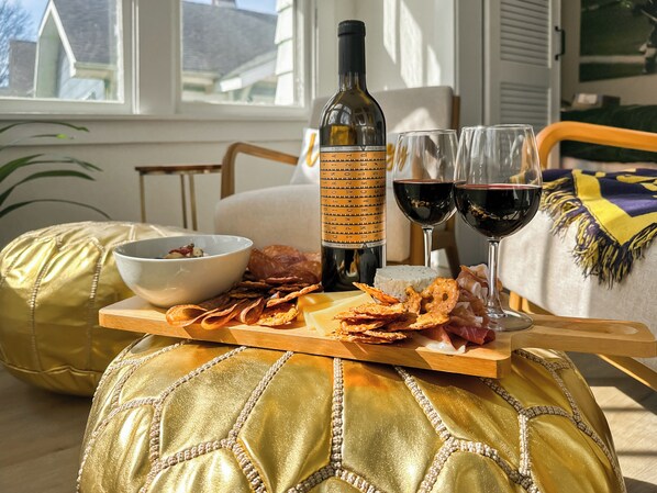 A dining table with a bottle of wine, glasses, cheese, crackers, and a bowl of food.