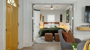 Un dormitorio con cama, almohadas, mesita de noche, televisión y puerta.