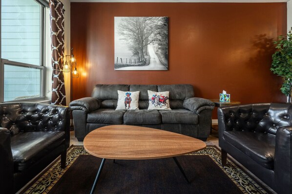 Ein modernes Wohnzimmer mit einem dunkelbraunen Ledersofa, einem Holztisch und einem großen abstrakten Gemälde an der Wand.