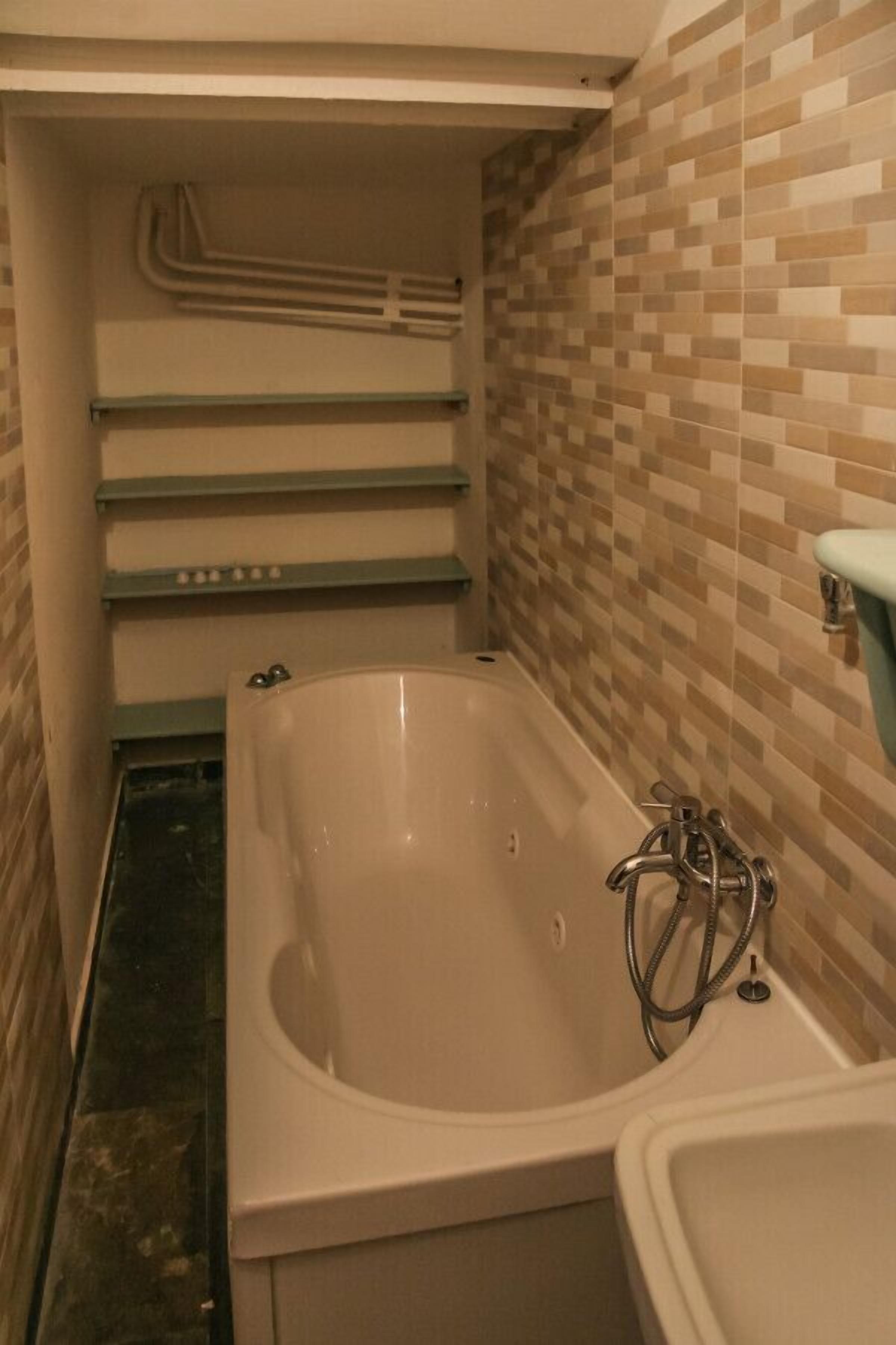 A bathroom with a bathtub, a shower, and a sink. There are tiled walls and a tiled floor.