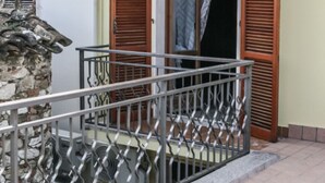 A balcony with a metal railing, a stone wall, and a window with wooden shutters. - Brothers Home: Italian Vacation (Civitella Casanova)