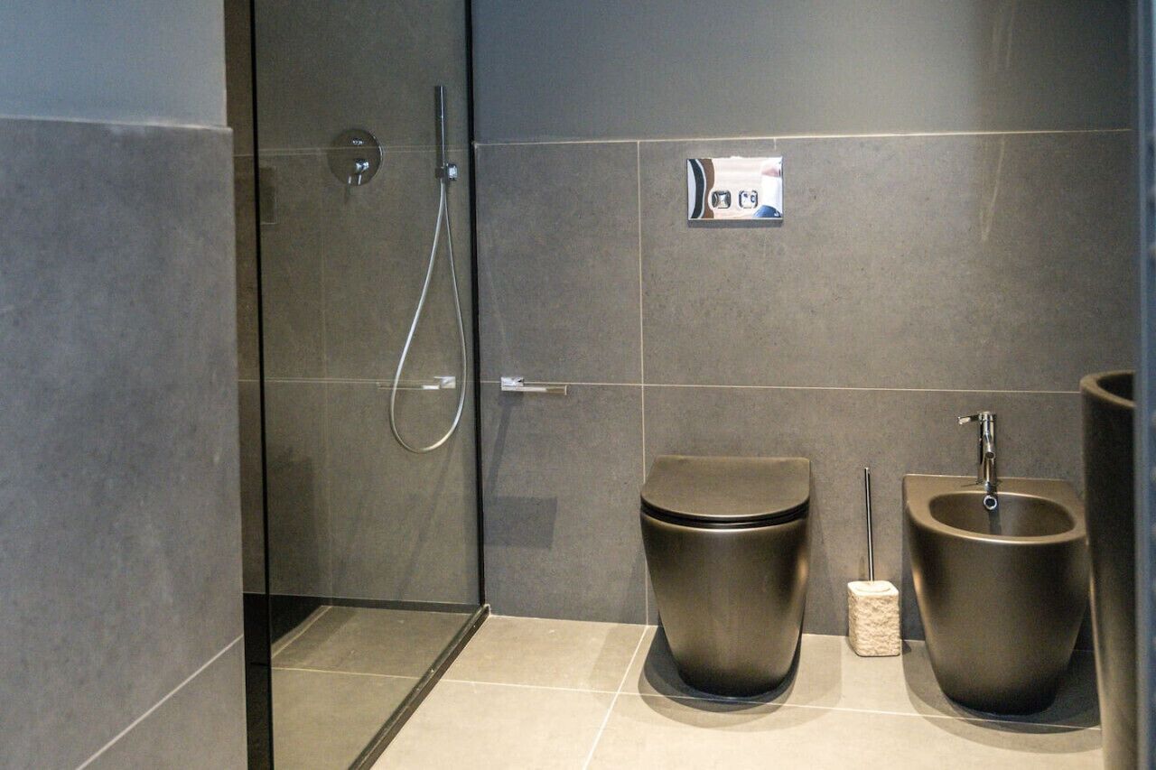 A modern bathroom with a shower, toilet, bidet, and a towel dispenser.