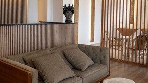 Een moderne woonkamer met een grijze bank, een houten bijzettafeltje en een decoratief buste op een plank.